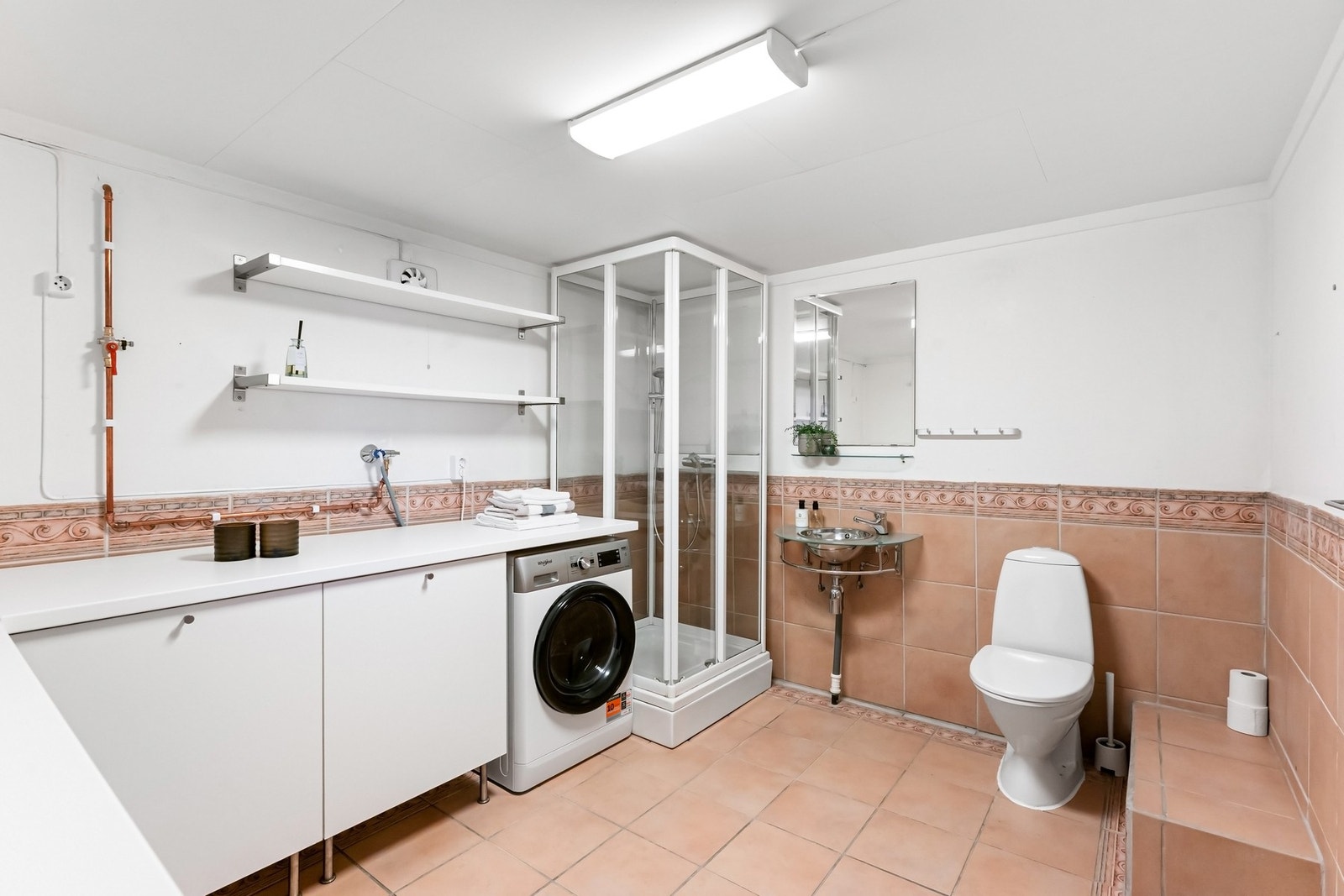 Romslig vaskerom innredet med dusjkabinett, toalett og servant og opplegg for vaskemaskin. God benkeplass med skap og hyller for oppbevaring. Galleribilde