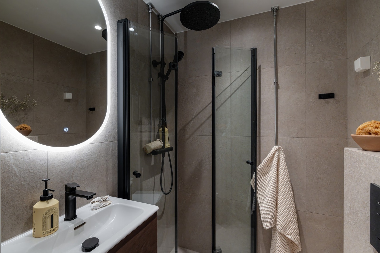 På badet er det innredning med glatte fronter og ovenpåliggende servant, samt speil med belysning rundt. Videre er det vegghengt toalett og regnfalldusj med innfellbare dusjdører. Galleribilde