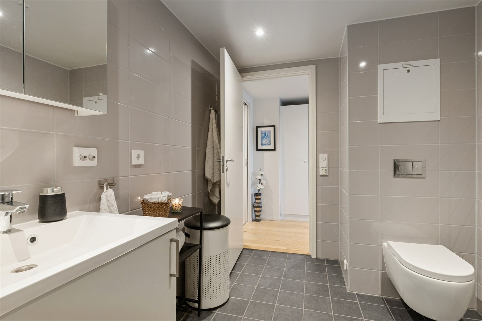 Lekkert flislagt bad/vaskerom med elektriske varmekabler i gulv, vegghengt toalett, svingbare dusjdører, servantskap og opplegg til vaskemaskin og tørketrommel. Galleribilde