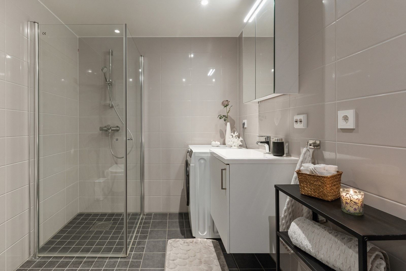 Lekkert flislagt bad/vaskerom med elektriske varmekabler i gulv, vegghengt toalett, svingbare dusjdører, servantskap og opplegg til vaskemaskin og tørketrommel. Galleribilde