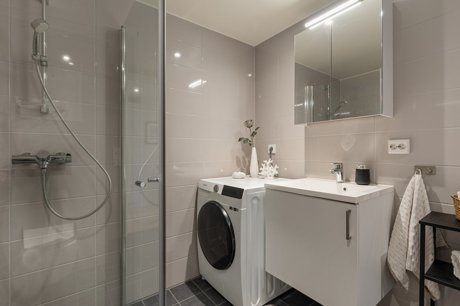 Lekkert flislagt bad/vaskerom med elektriske varmekabler i gulv, vegghengt toalett, svingbare dusjdører, servantskap og opplegg til vaskemaskin og tørketrommel. Galleribilde