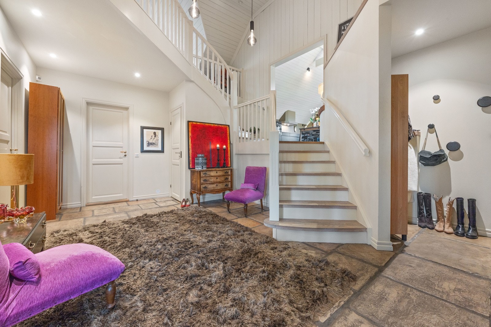 Første møtet med huset er en romslig hall med takhøyde på inntil ca. 5,25 meter, hvitmalt trapp med avsats til kjøkken og pendelbelysning. Dette rommet gir et godt førsteinntrykk av boligens størrelse og utforming. Galleribilde