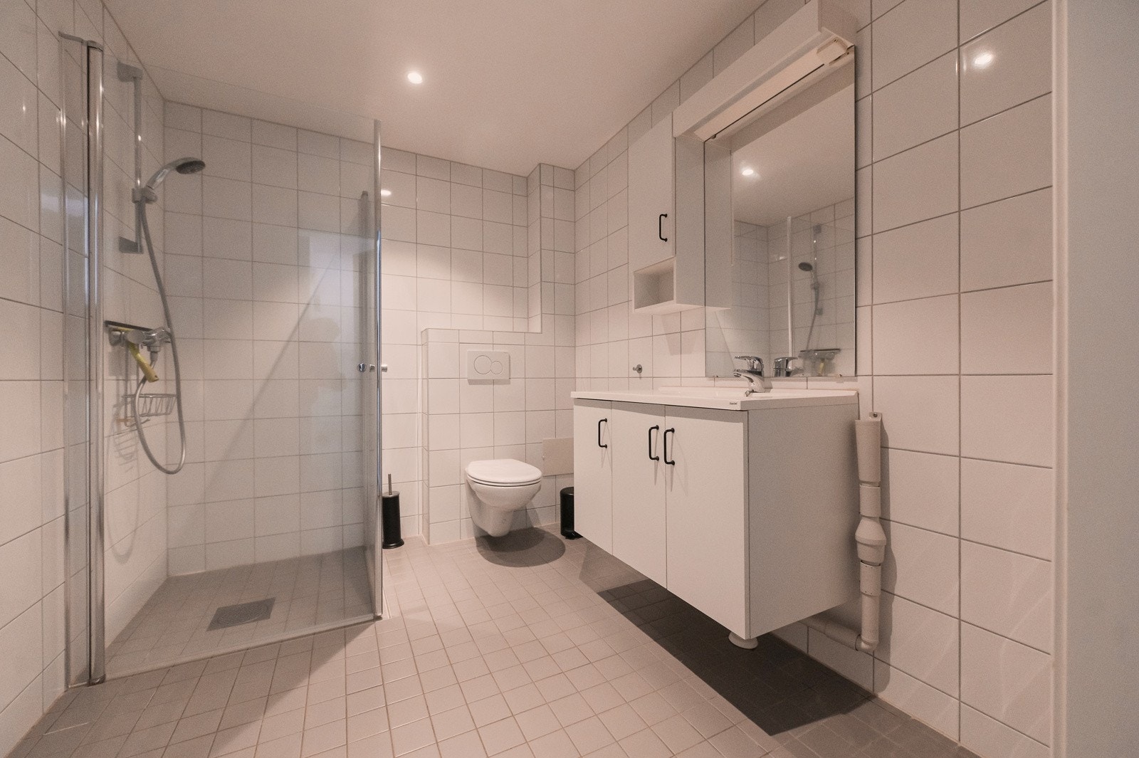 Lyst flislagt bad med varme i gulvet. Vegghengt servantinnredning, dusjhjørne med dører og vegghengt toalett. Opplegg for vaskemaskin. Galleribilde