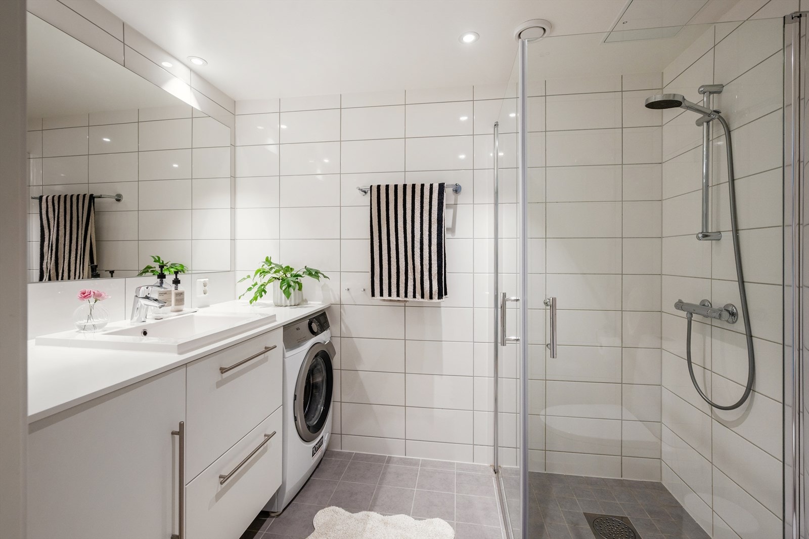 Praktisk og stilren bad med vegghengt klosett, servant nedfelt i laminat benkeplate med god skapplass samt speil. Dusjhjørne med svingbare glassdører gir en åpen og funksjonell løsning. Galleribilde