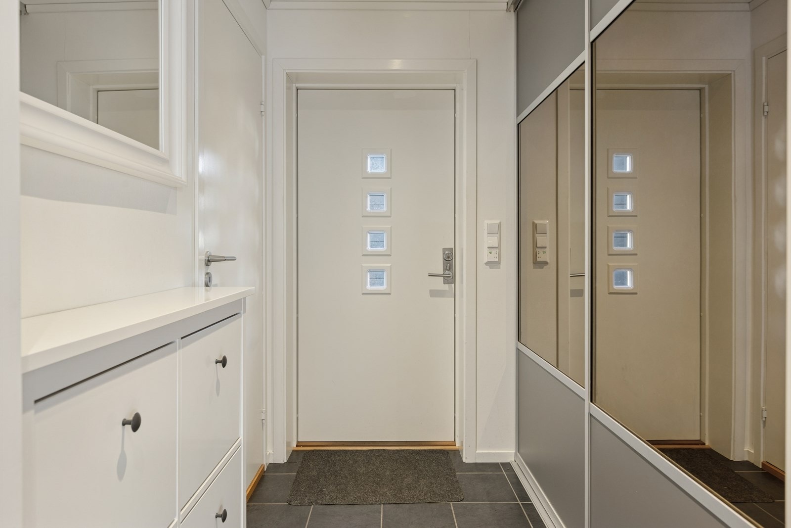 Man ønskes velkommen inn i en lys entré som er praktisk innredet med flislagt gulv og stor skyvedørsgarderobe med god lagringsplass til familiens yttertøy. Galleribilde