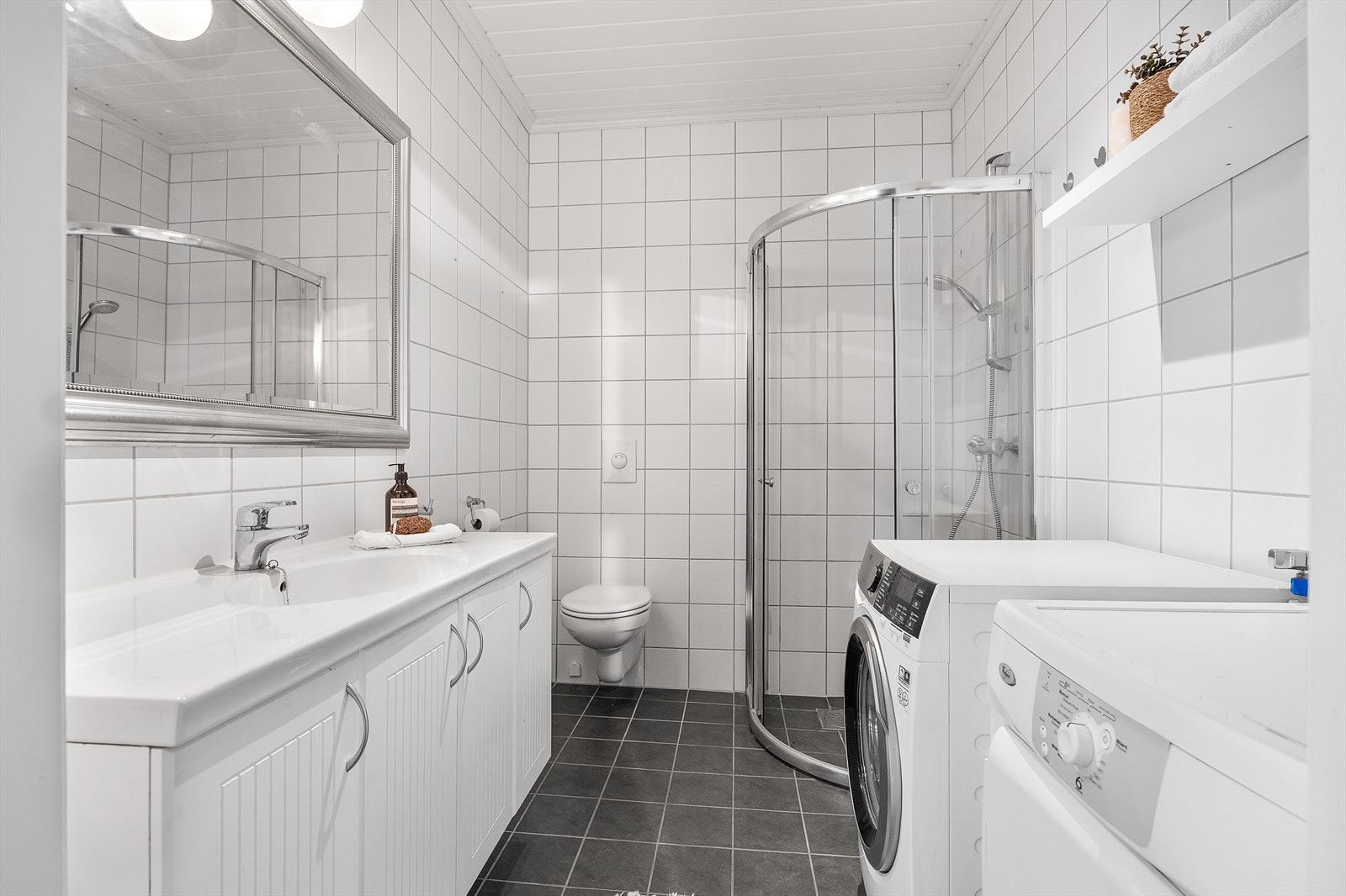 Det helflisede og delikate badet har innredning med stor servantbenk over hvite underskap, og et sølvfarget speil med tilhørende lys. Galleribilde