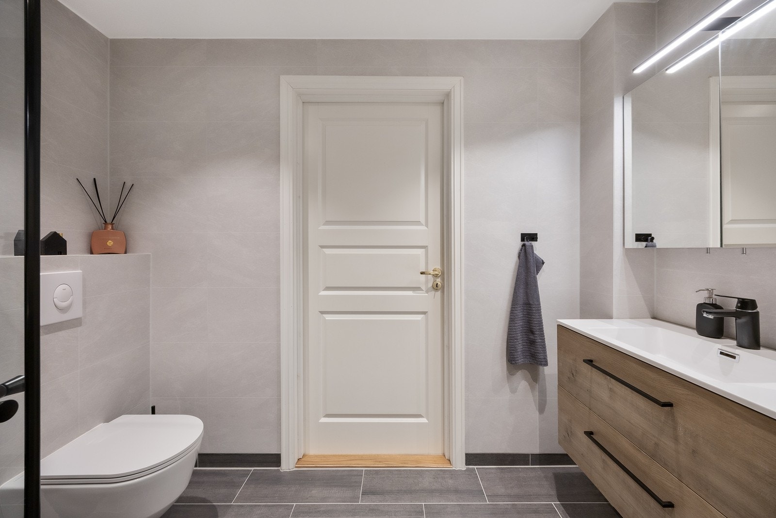 Videre har badet vegghengt toalett, dusjhjørne utstyrt med slukrenne, sort regnfallsdusj og innfellbare glassdører i sort innramming - samt varme i gulvet. Galleribilde