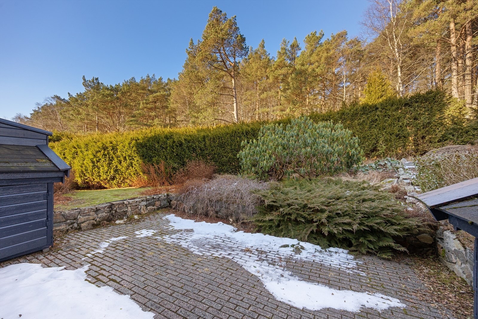 Stor uteplass på baksiden med ca 23 m² dekke med belegningstein. Opp mot friområdet i bakkant går en stor hekk som skjermer for innsyn. Mellom uteplassen og hekken er det anlagt bed med busker som også kan innlemmes i uteplassen Galleribilde