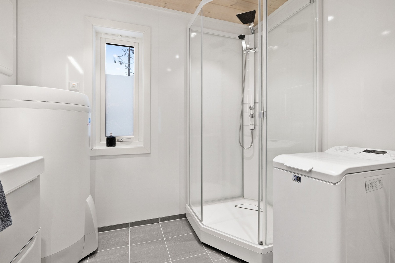 Baderommet er utstyrt med vegghengt toalett, baderomsinnredning, dusjkabinett og opplegg for vaskemaskin Galleribilde