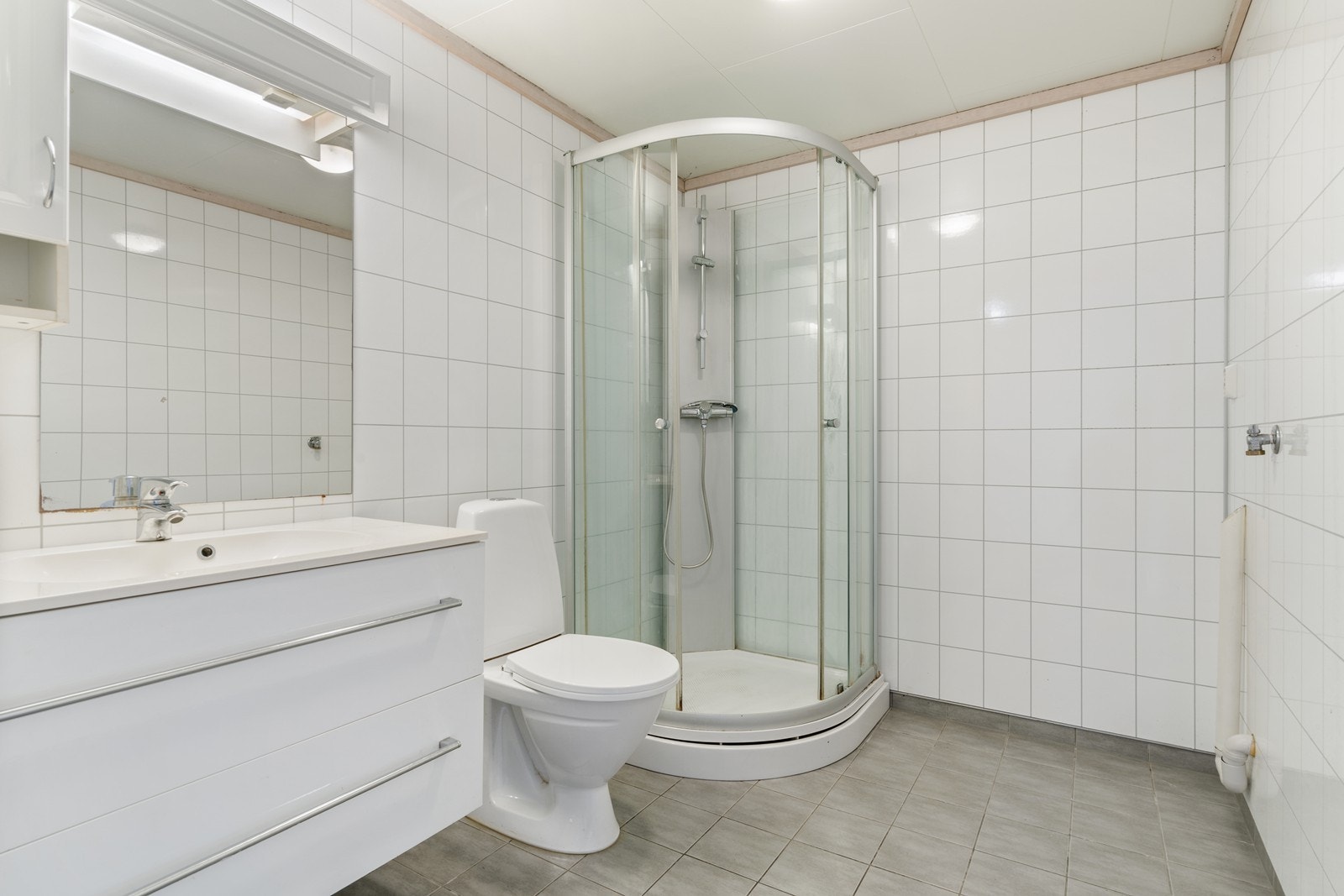 Bad med fliser på gulv, varmekabler, dusjkabinett og vaskesøyle Galleribilde