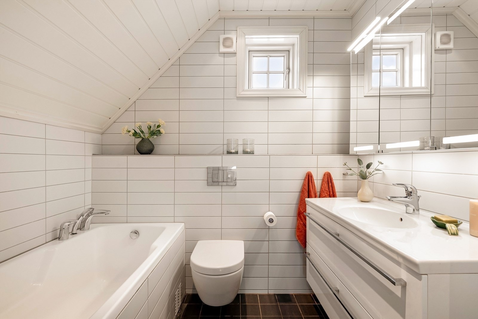 Delikat bad innredet med flislagt badekar, servantskap, speilskap og vegghengt klosett Galleribilde