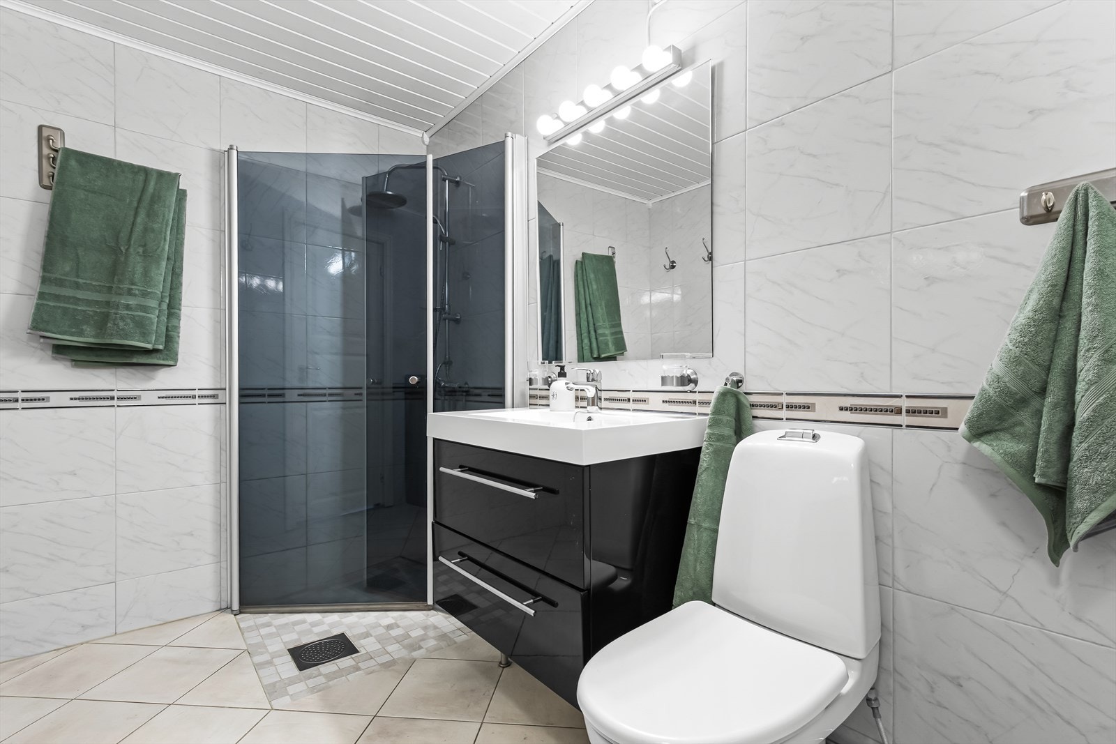 Badet fremstår lyst, romslig og innbydende med funksjonelle overflater. Gulvet er flislagt med elektriske varmekabler som gir behagelig varme. Galleribilde