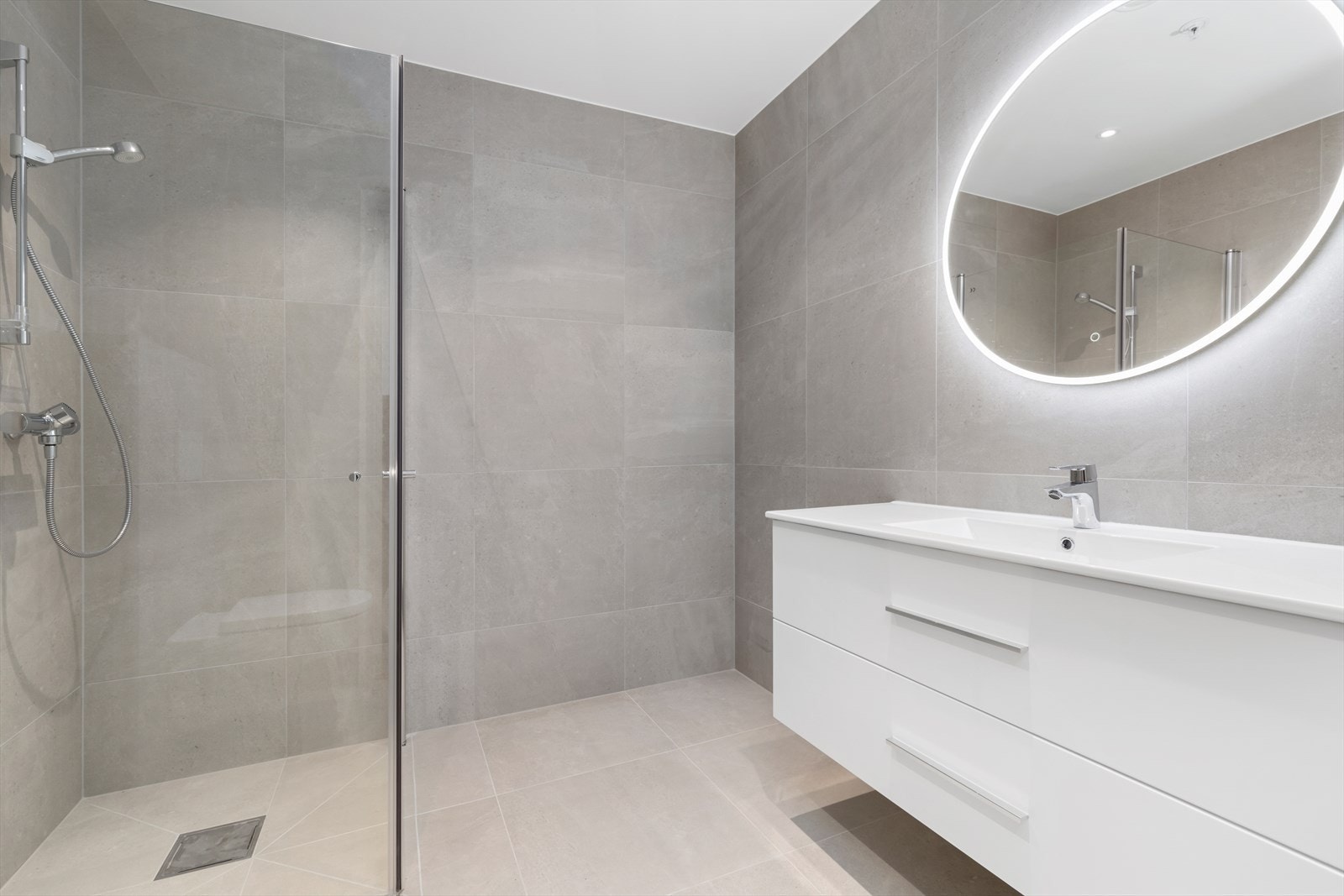 Helfliset bad med 60*60 flis, vegghengt toalett, stor dusjnisje og praktisk baderomsinnredning. Galleribilde