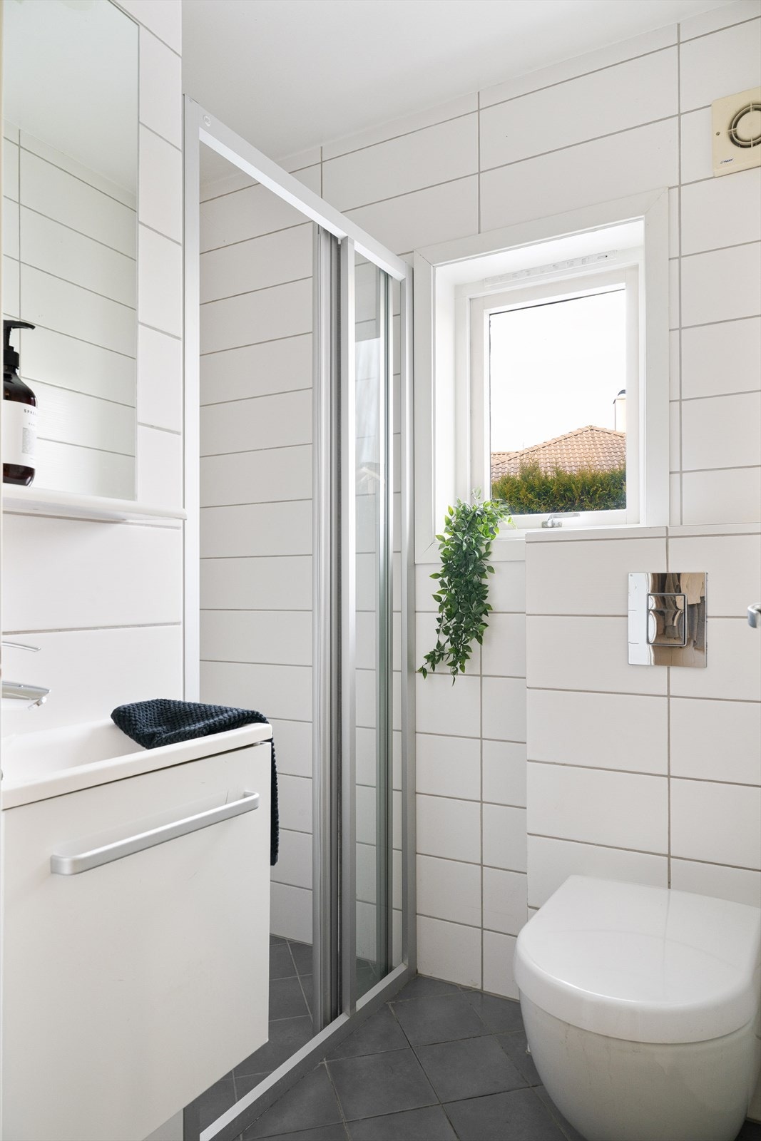 Pent flislagt bad med dusjløsning, servantinnredning og vindu som gir naturlig lys. Galleribilde