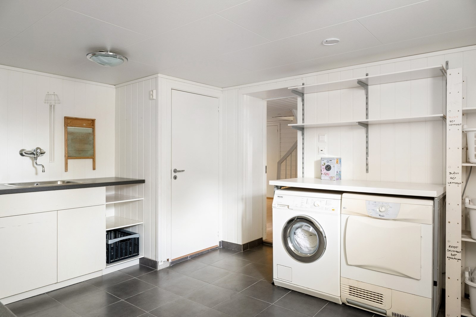 Praktisk og romslig vaskerom med opplegg for vaskemaskin og tørketrommel, gode benkeflater, utslagsvask og rikelig med skap- og hylleplass. Galleribilde