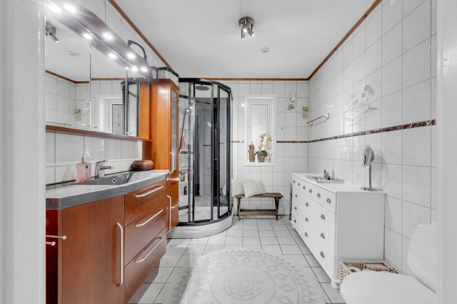 Bad som er flislagt md lyse fliser. Stor baderomsinnredning med lyssatt speil. Galleribilde