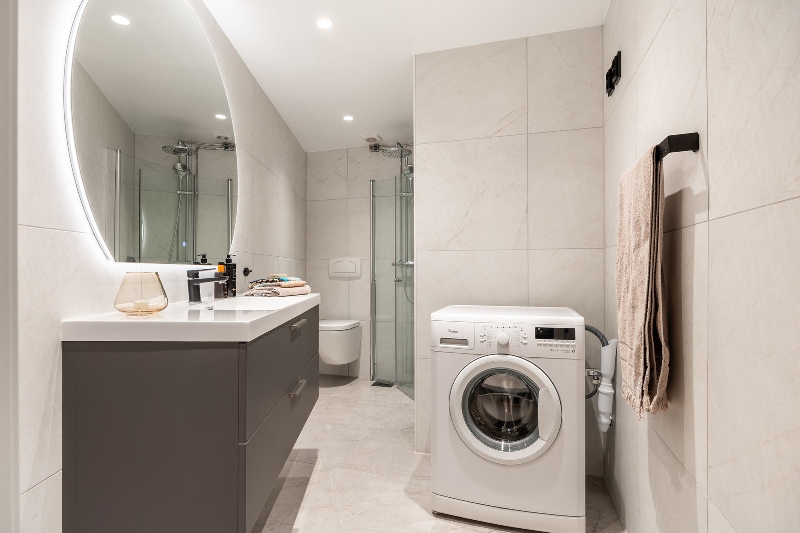 Lyst og pent baderom med flislagt gulv med gulvvarme og opplegg for vaskemaskin. Galleribilde