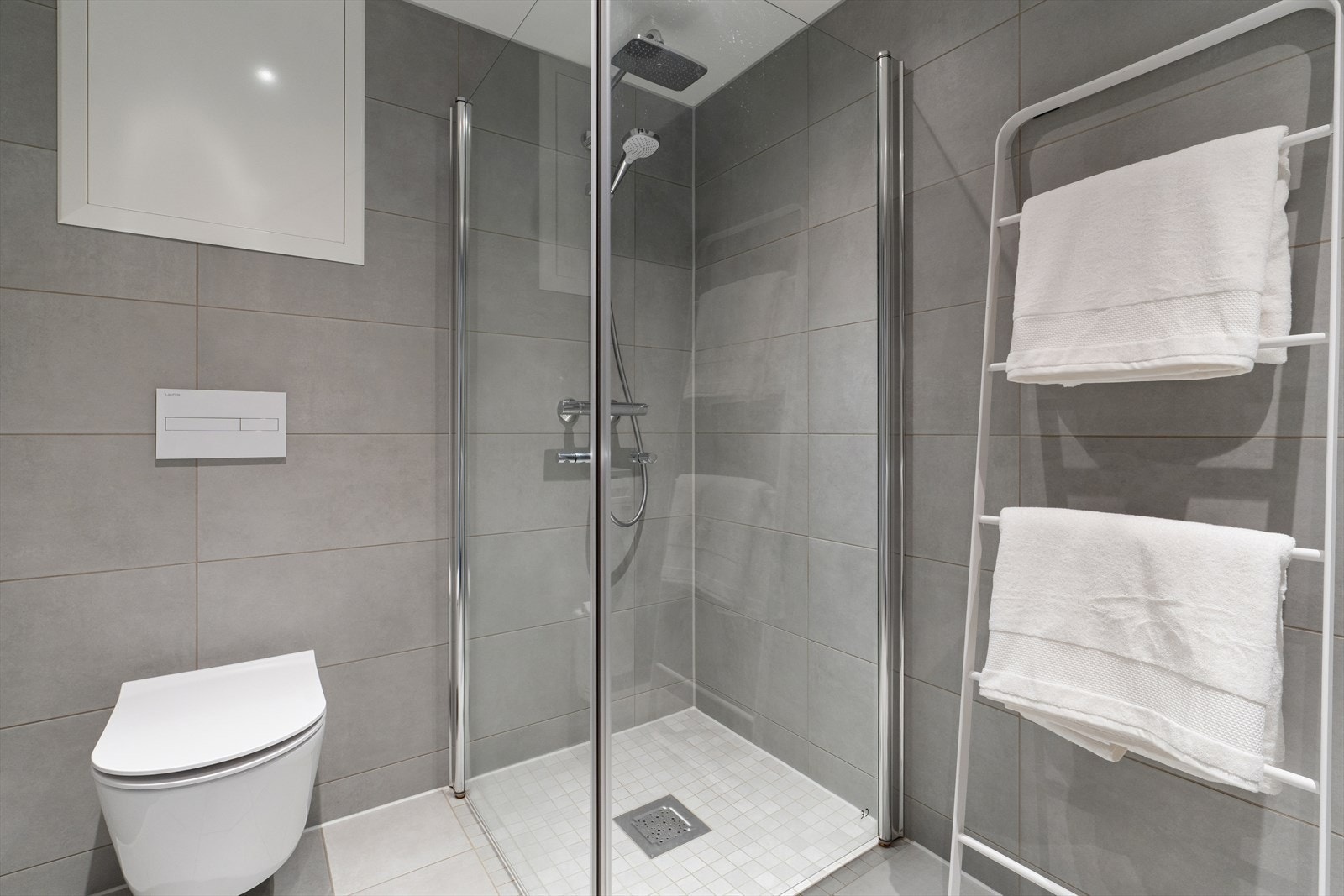 Badet er innredet med vegghengt toalett, dusjhjørne med svingbare glassdører og servant med praktisk skuffeinnredning. Galleribilde