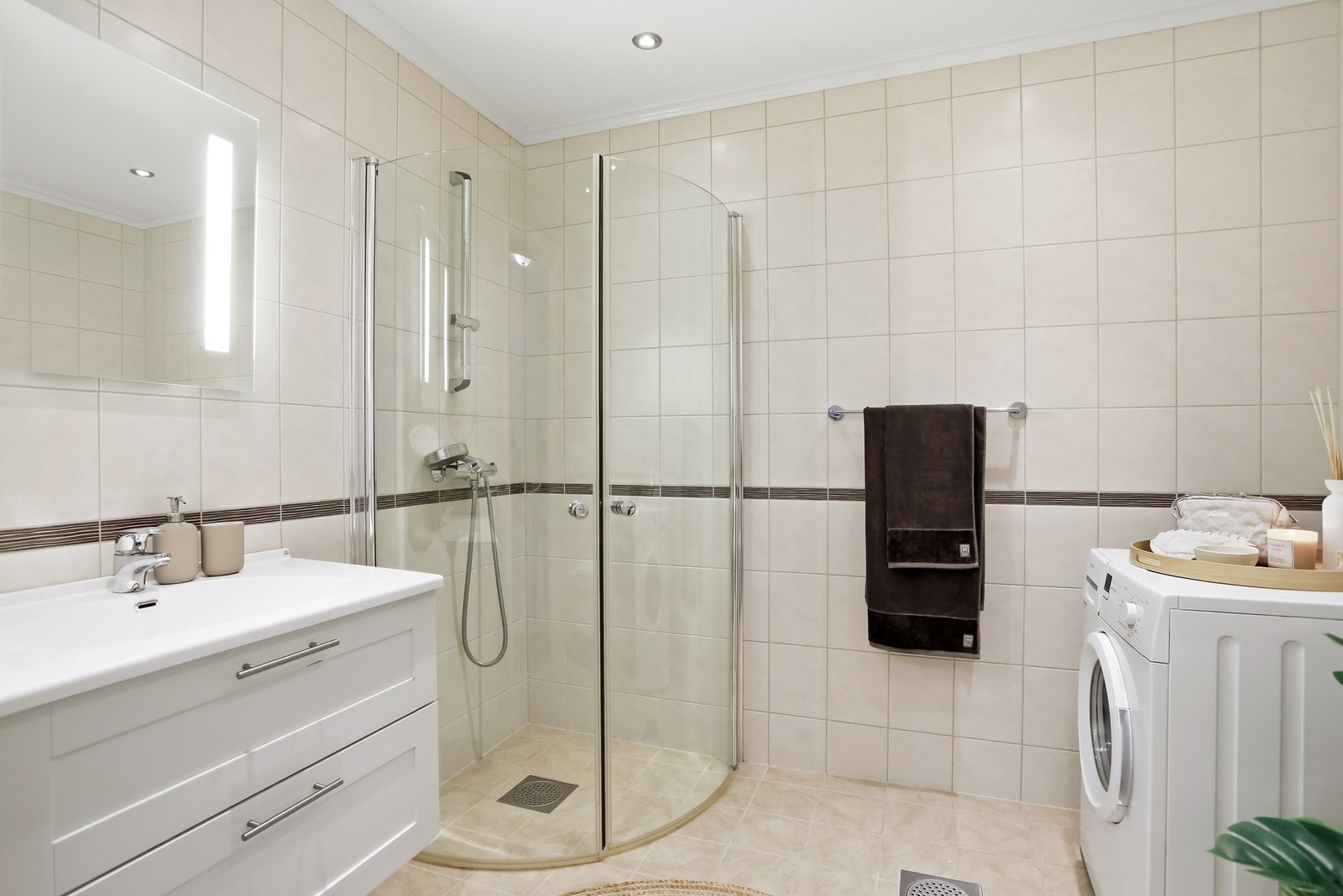 Lekkert, flislagt bad av god størrelse med vegghengt toalett, montert dusjnisje, servant på innredning samt opplegg for vaskemaskin og tørketrommel. Galleribilde