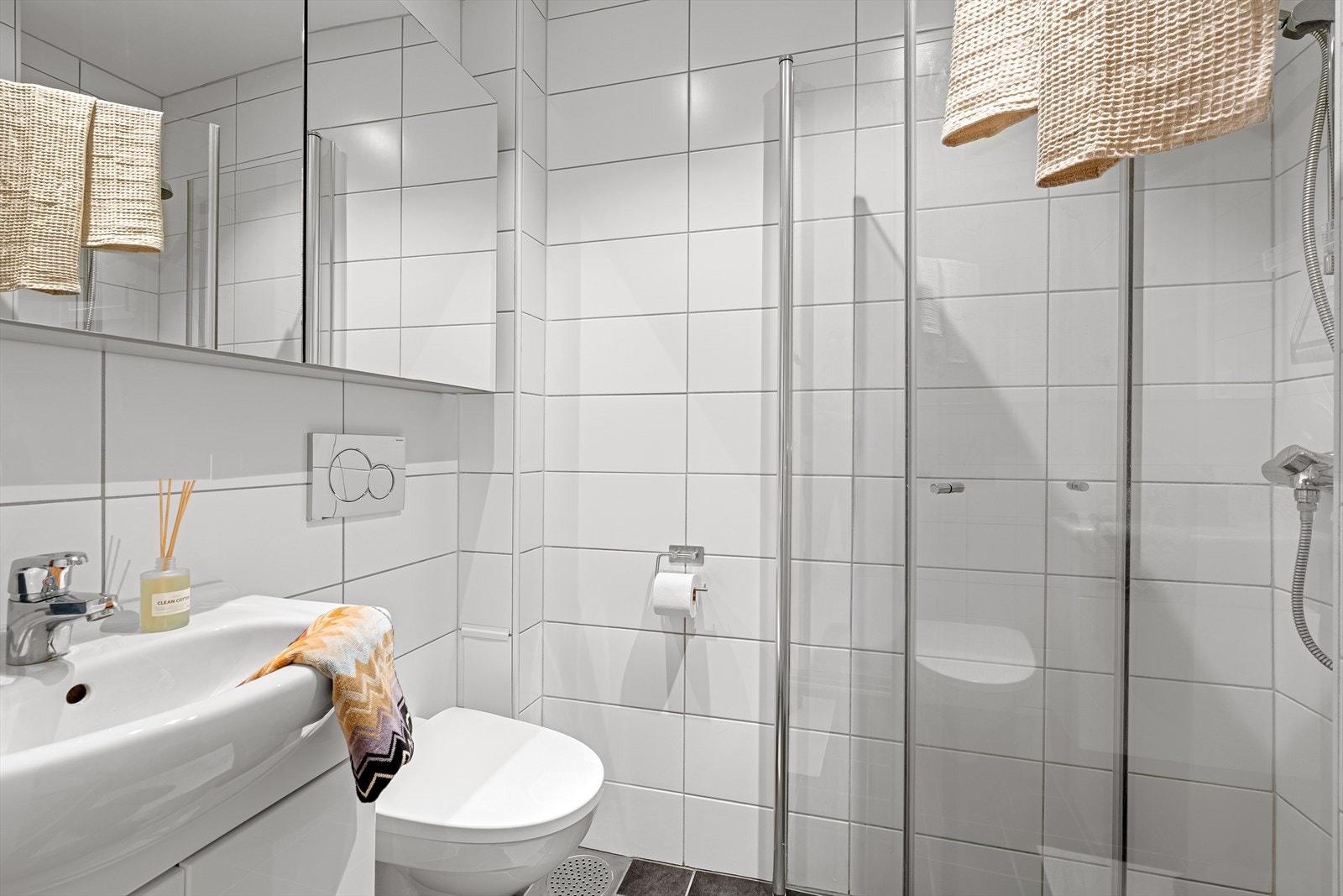 Flislagt bad med vegghengt toalett, servant med innredning og dusjhjørne Galleribilde