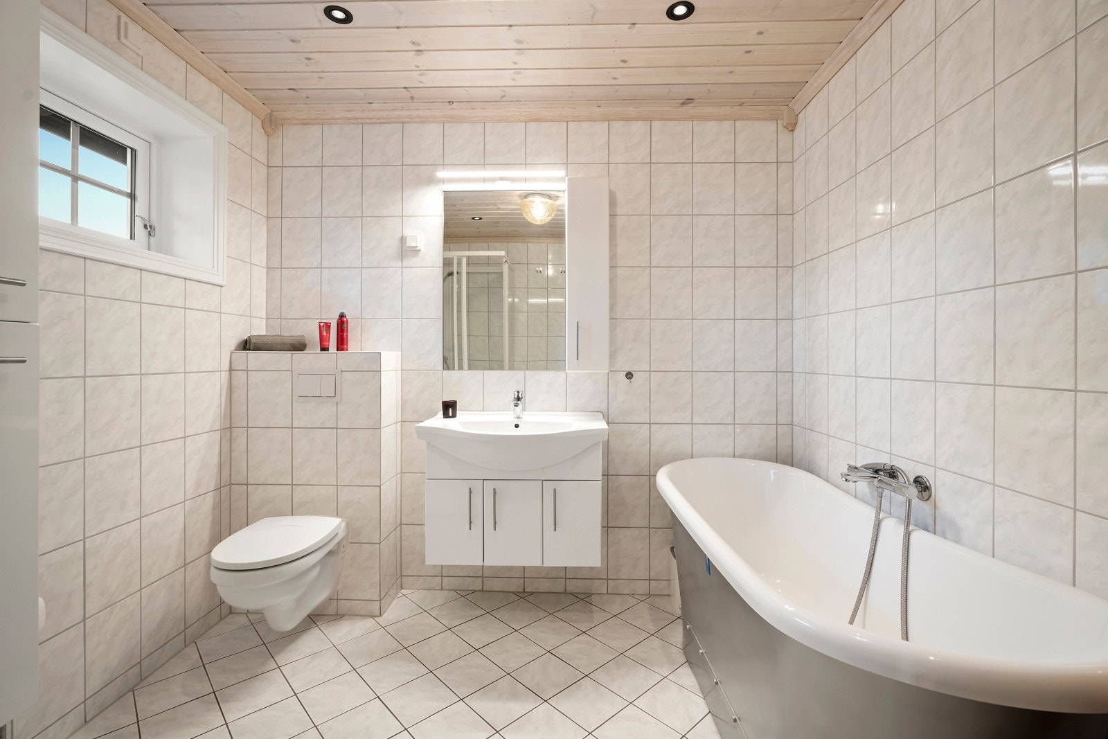 Badet er innredet med nedfelt servant, speil med belysning, veggmontert toalett, dusjkabinett og badekar. Galleribilde