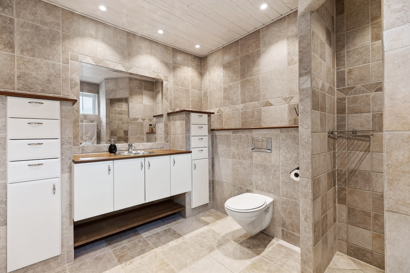 Lekkert og romslig bad med både badekar, en flott dusjnisje, vegghengt toalett, stor servantinnredning og godt med skap og skuffer for oppbevaring. Galleribilde