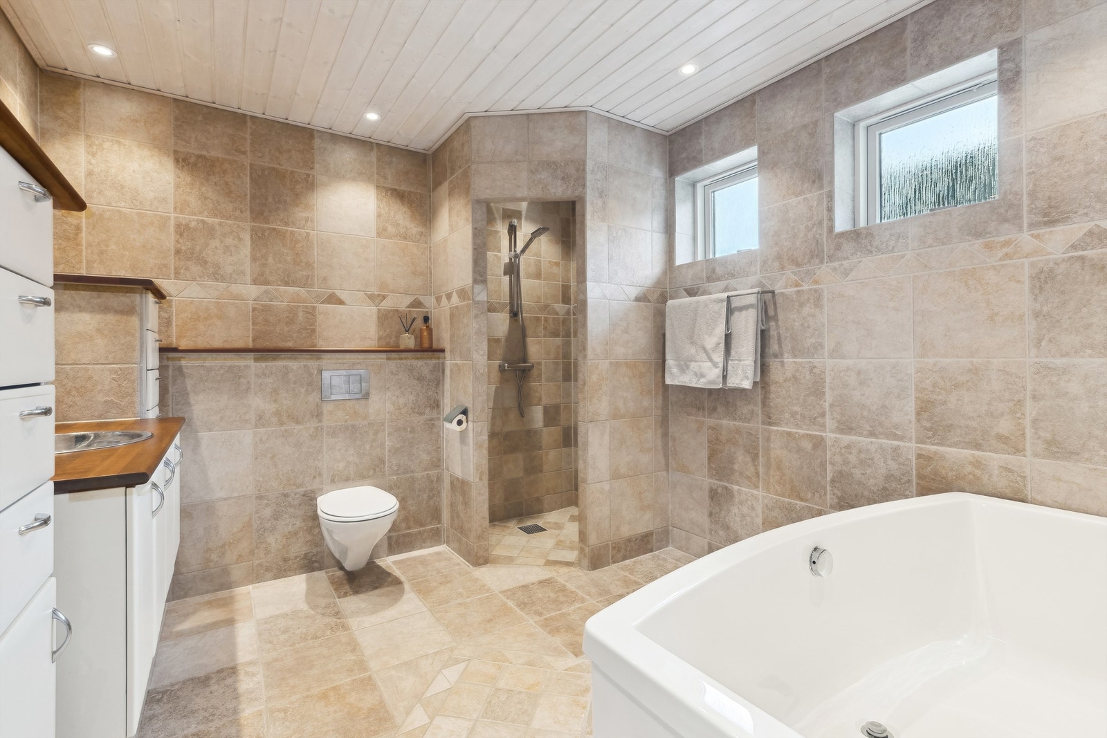 Lekkert og romslig bad med både badekar, en flott dusjnisje, vegghengt toalett, stor servantinnredning og godt med skap og skuffer for oppbevaring. Galleribilde