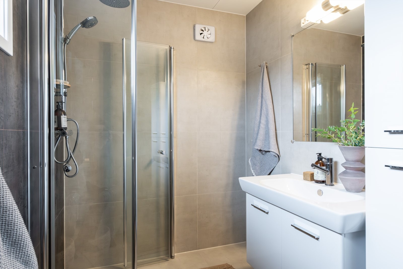 Innredningen består av servantskap med heldekkende servantplate på hvitmalt skuffeseksjon, speil og toalett. Det er en fin dusjnisje med innfellbare glassdører og regnfallsdusj. Galleribilde