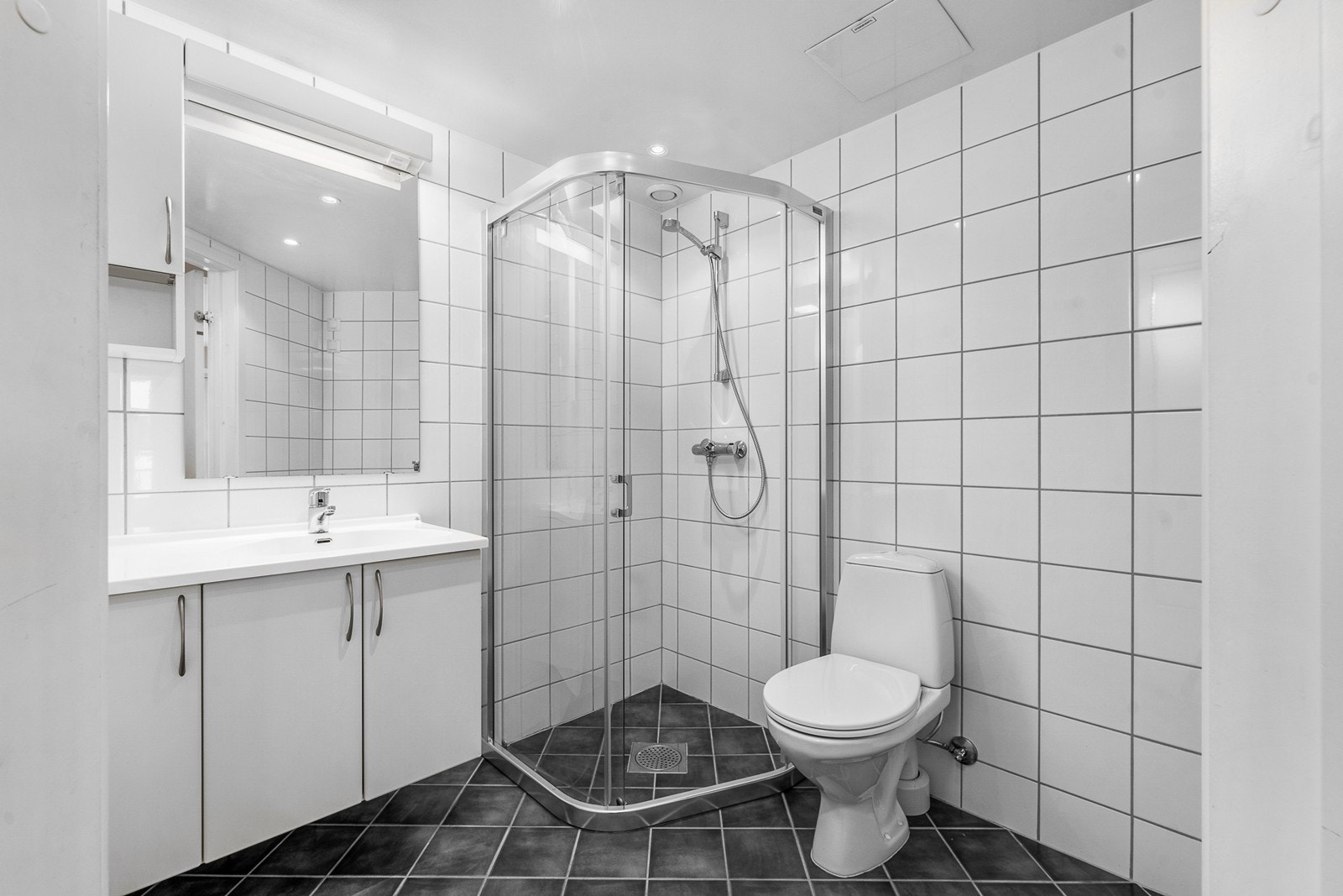 Flislagt bad med mørke gulvfliser som gir en fin kontrast til de hvite veggflisene. Galleribilde