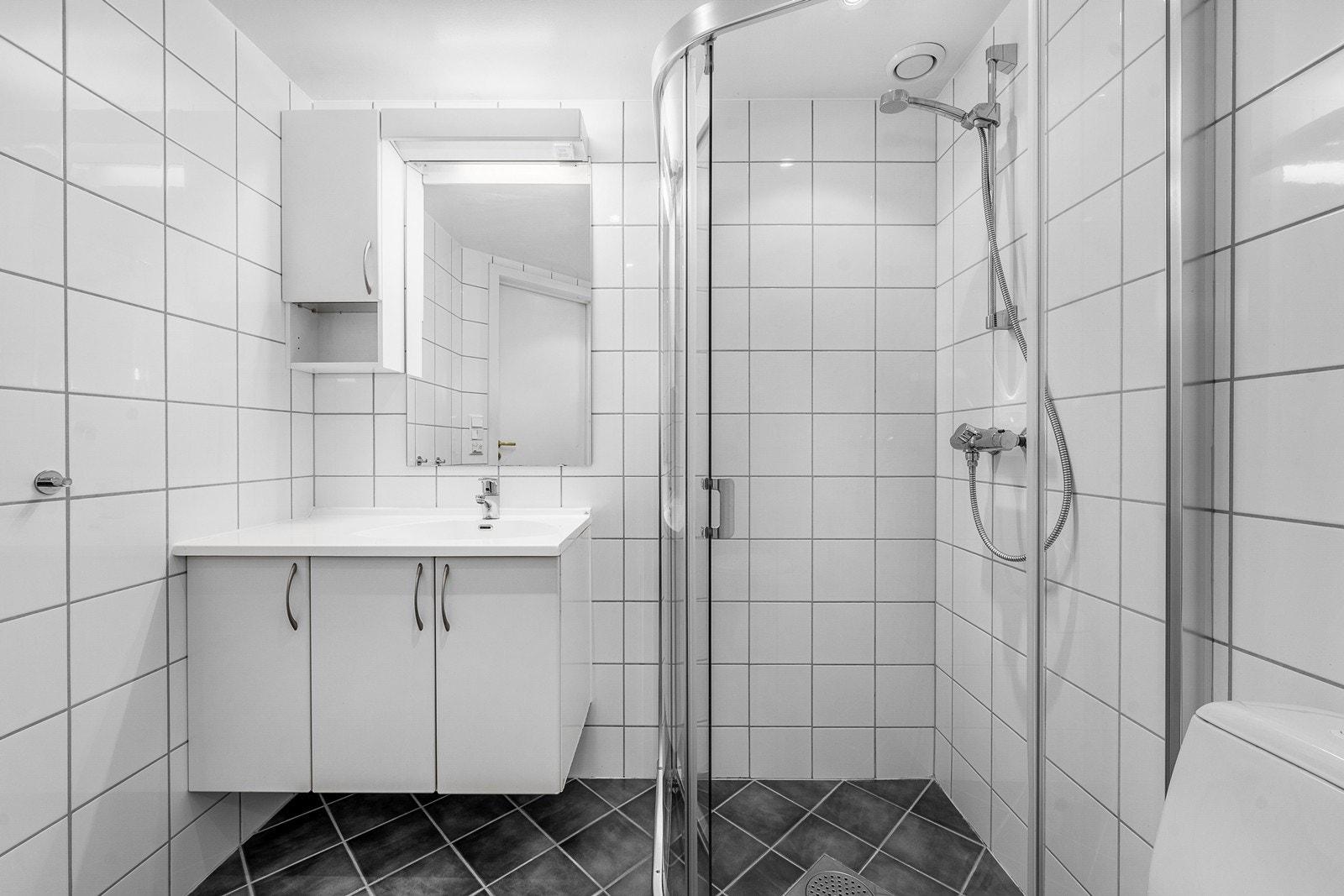 Badet er innredet med servantmøbel, toalett og et dusjhjørne. Galleribilde