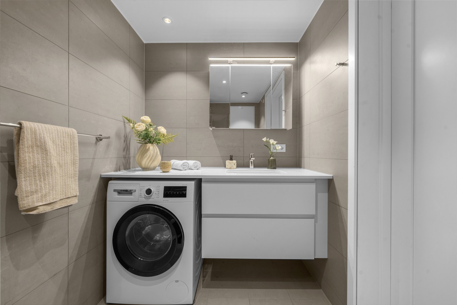 Videre er badet utstyrt med dusjhjørne i herdet glasss, vegghengt toalett og praktisk innrending og opplegg for vaskemaskin. Galleribilde