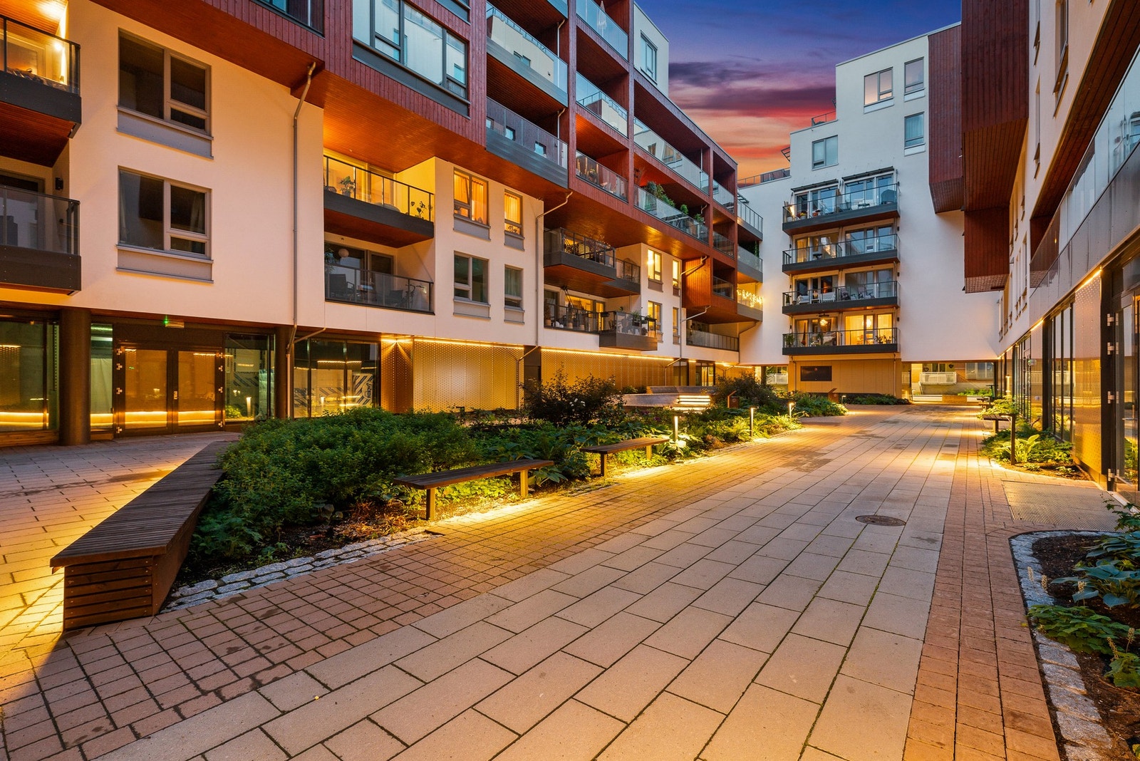 Delikat og moderne uteområde med stemningsfull kveldsbelysning, beplatning og sitteplasser. Galleribilde