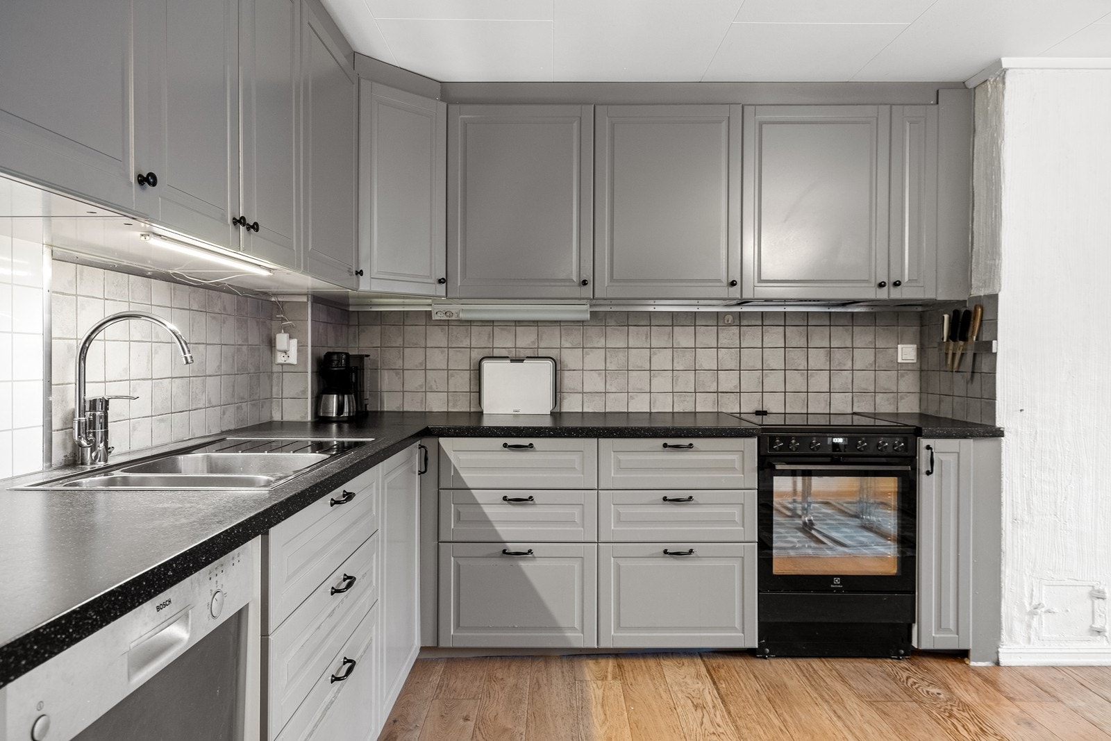 Grå fronter og mørk benkeplate. Fliser over benk. Galleribilde