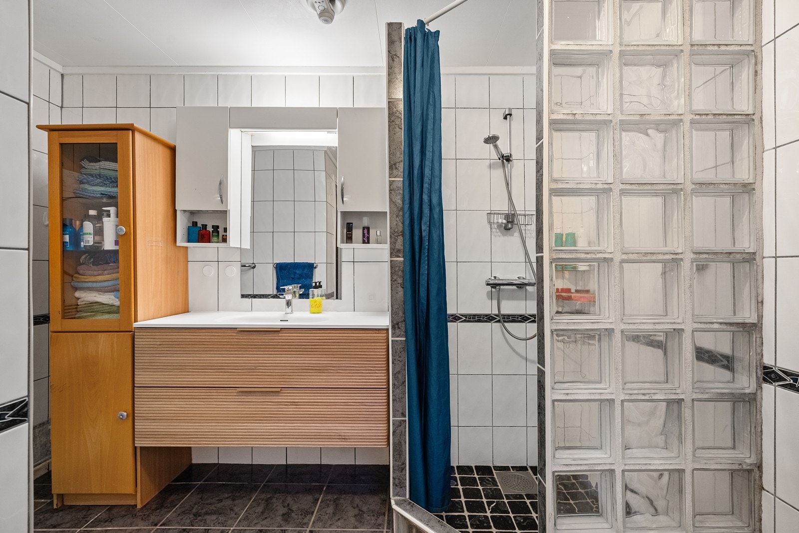 Flisebelagt bad med nyere vask i seksjon og speil. Galleribilde