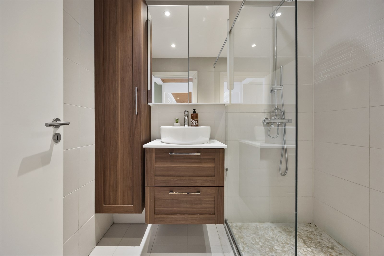 Badet har fliser på gulv og vegger, svevende servant, speilskap, vegghengt skap og dusj med glassvegg. Galleribilde