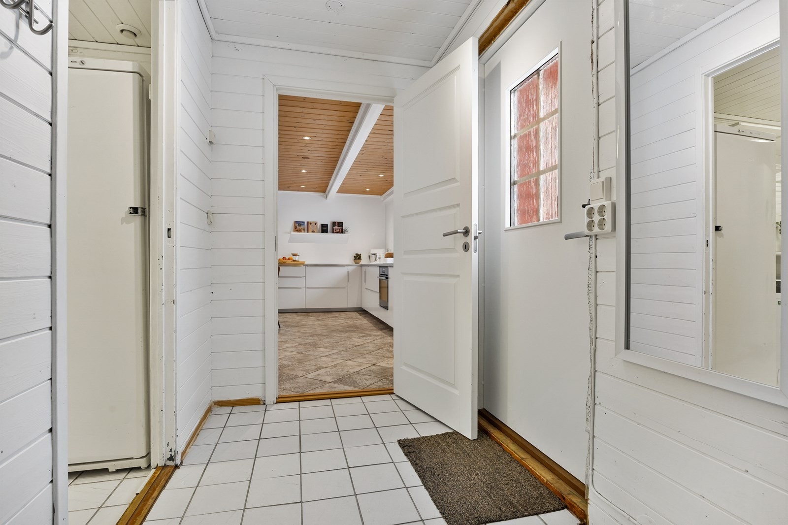 Enkel inngang med flislagt gulv og trepanel på veggene. Galleribilde