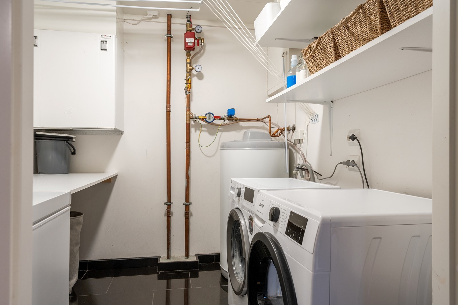 Praktisk vaskerom med flislagt gulv, opplegg for vaskemaskin, oppbevaringshyller og balansert ventilasjon Galleribilde