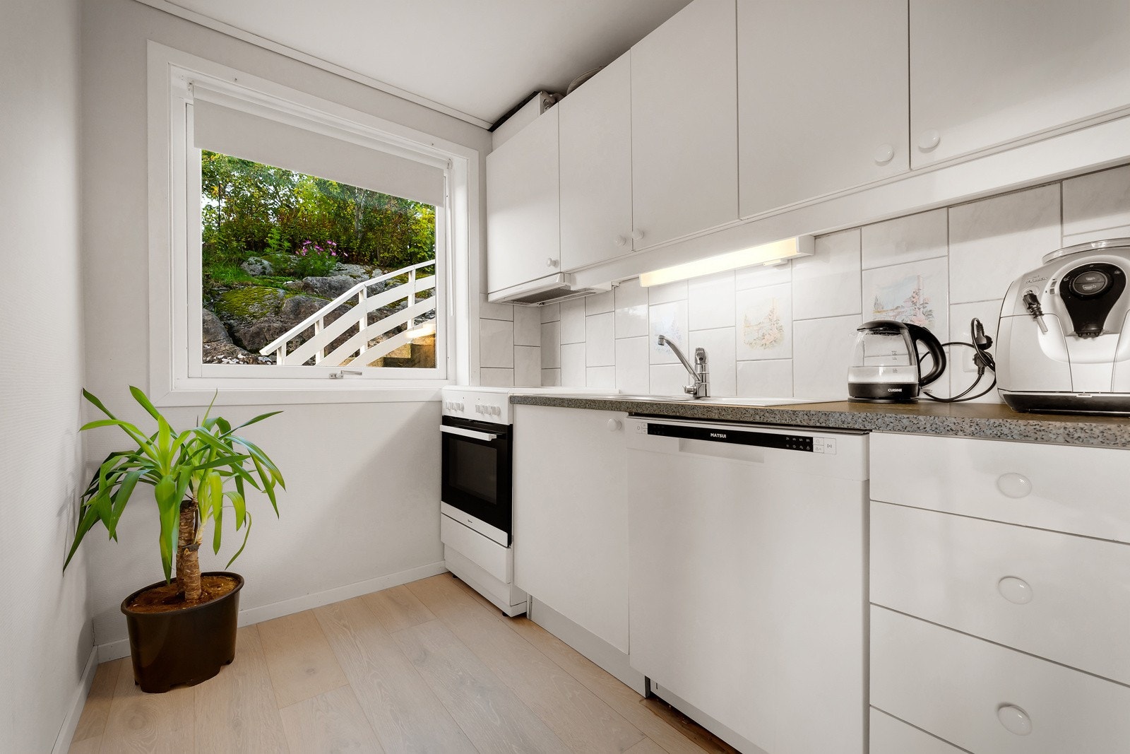 Flott og lyst kjøkken innredet med hvite glatte fronter og laminert benkeplate med kjøkkenbeslag. Galleribilde