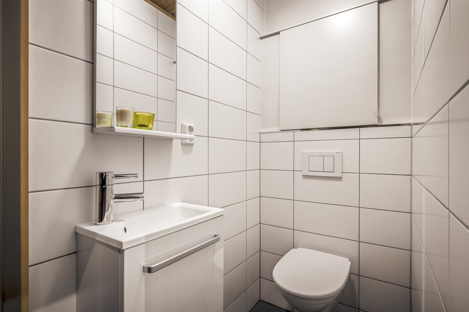 Praktisk separat toalettrom med vegghengt toalett, servant med skap og fliser på gulv og vegger. Varmekabler i gulv. Galleribilde