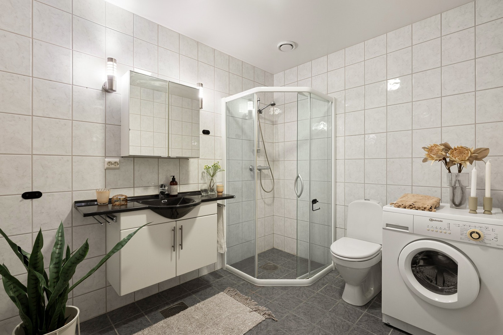 Romslig, helfliset bad med varme i gulv. Badet er innredet med hvit baderomsinnredning med mørk servantplate og tilhørende speilskap. Galleribilde