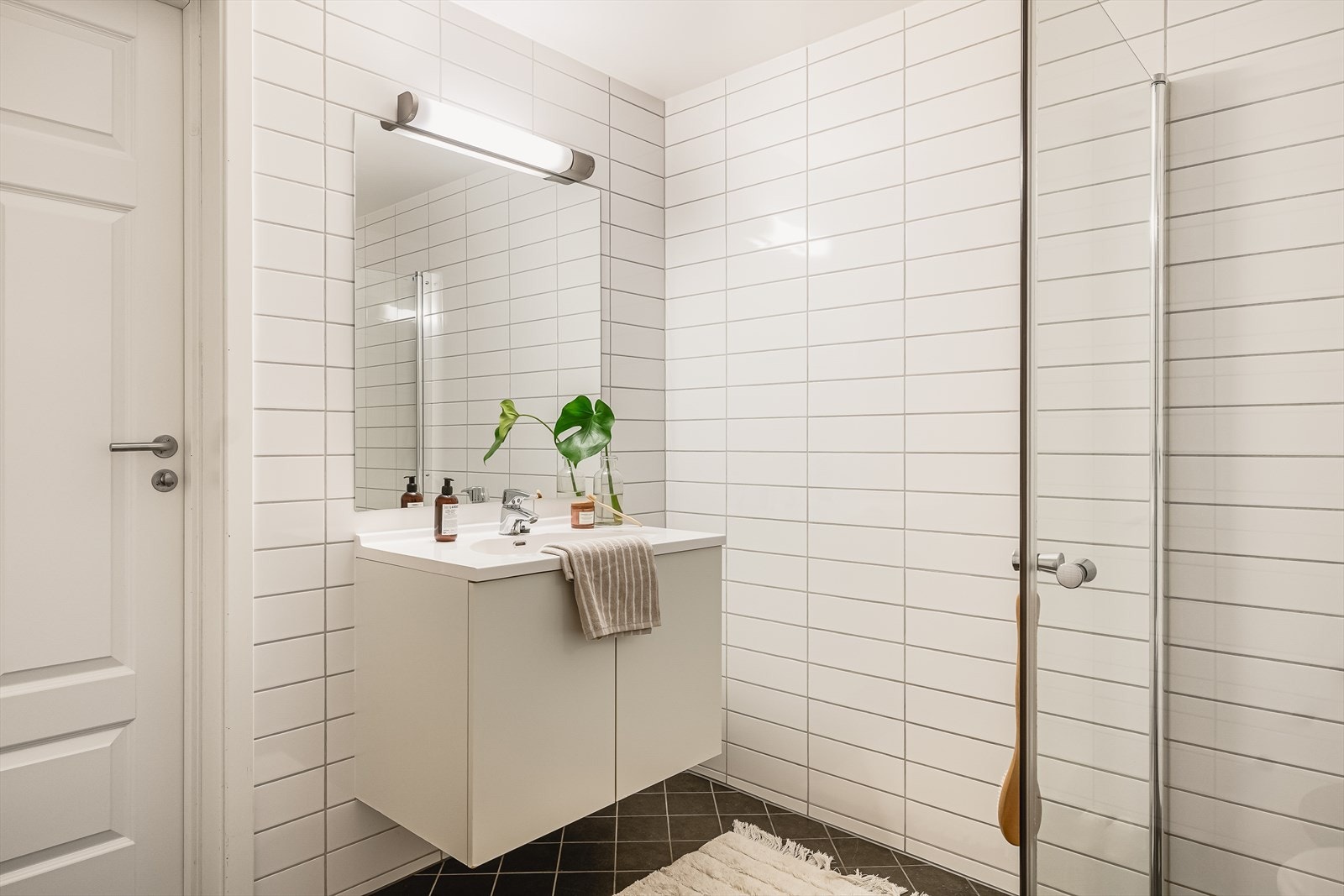 Badet inneholder servant med møblement, speil og belysning, vegghengt toalett samt innfellbart dusjhjørne i glass med tilhørende dusjgarnityr. Galleribilde