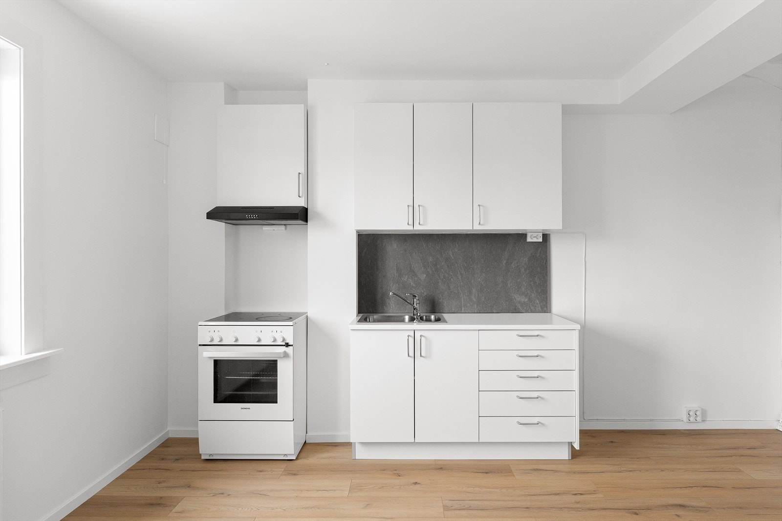 Innredningen består av glatt, laminert kjøkkeninnredning, plater mellom overskap og laminert benkeplate, kum med ettgreps blandebatteri og kullfiltervifte over komfyr Galleribilde