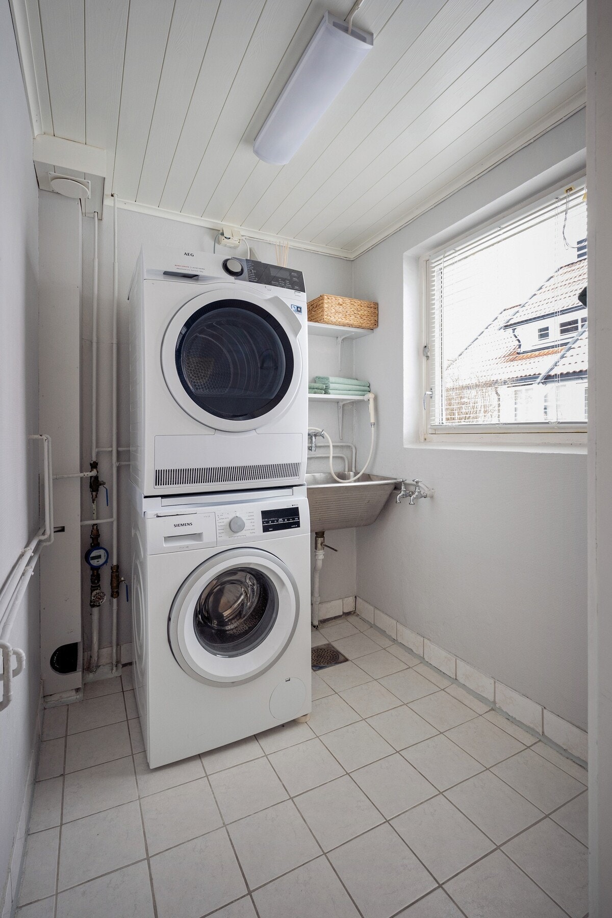 Praktisk og funksjonelt vaskerom med flislagt gulv og opplegg for vaskemaskin og tørketrommel. Galleribilde