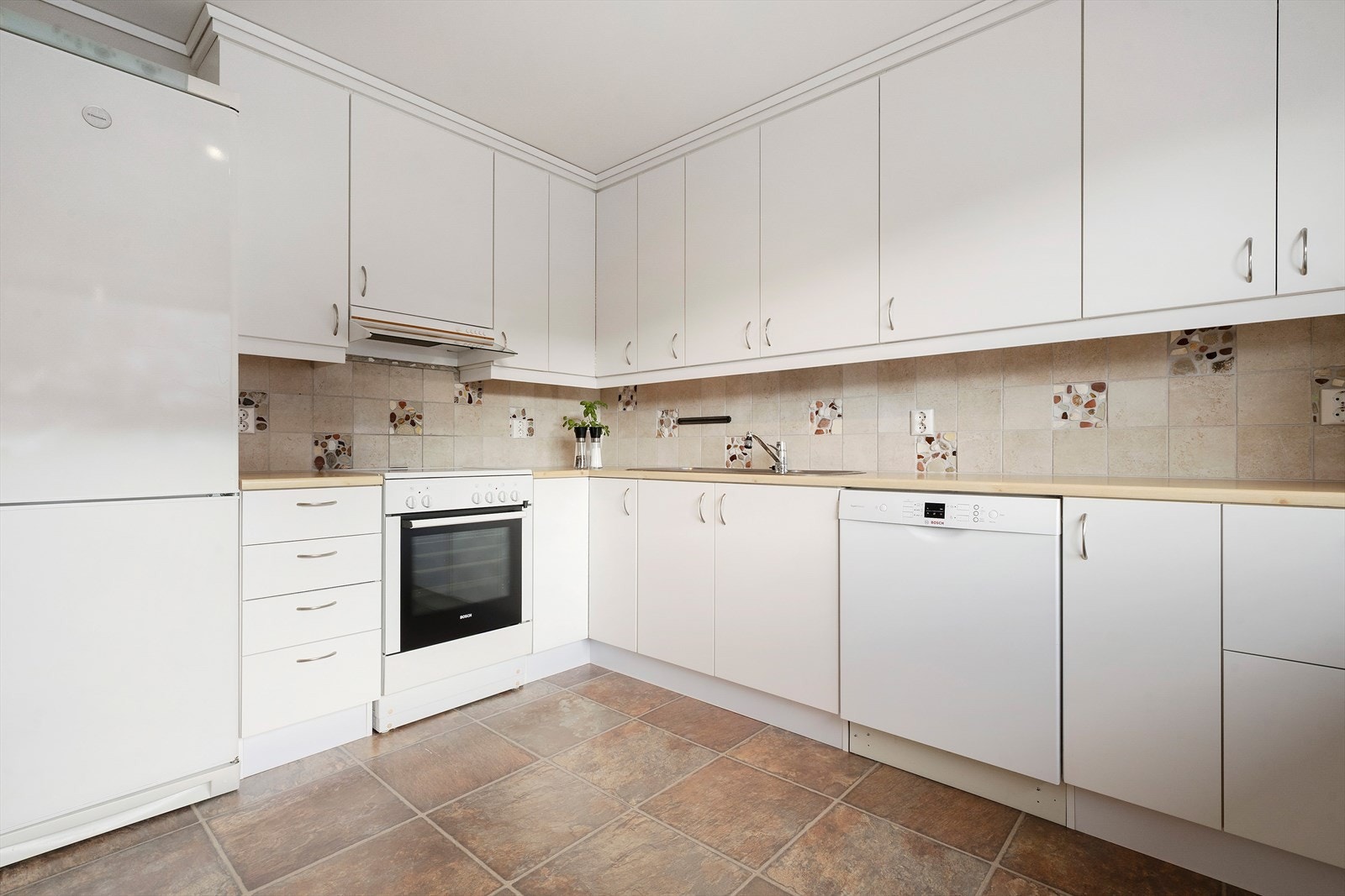 Innreiing med kvite slette frontar, laminert benkeplate og fliser mellom over- og underskap Galleribilde