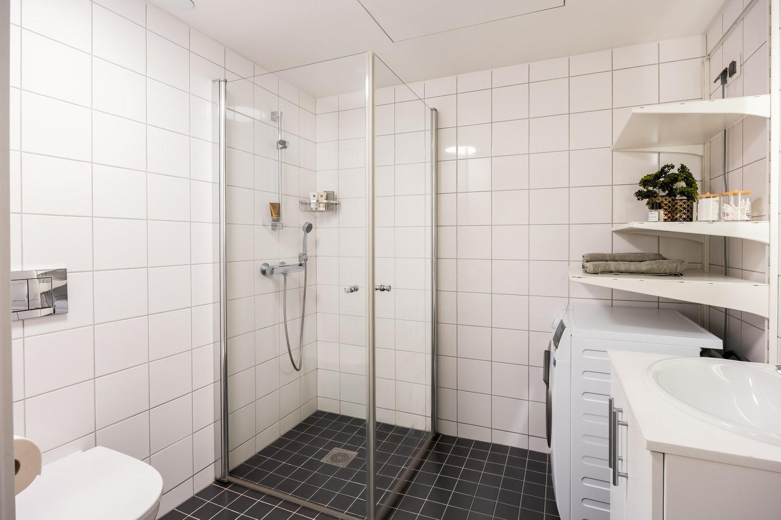 Badet er innredet med dusjvegger av glass, vegghengt toalett, servant med underskap, samt opplegg for vaskemaskin og tørketrommel. Galleribilde