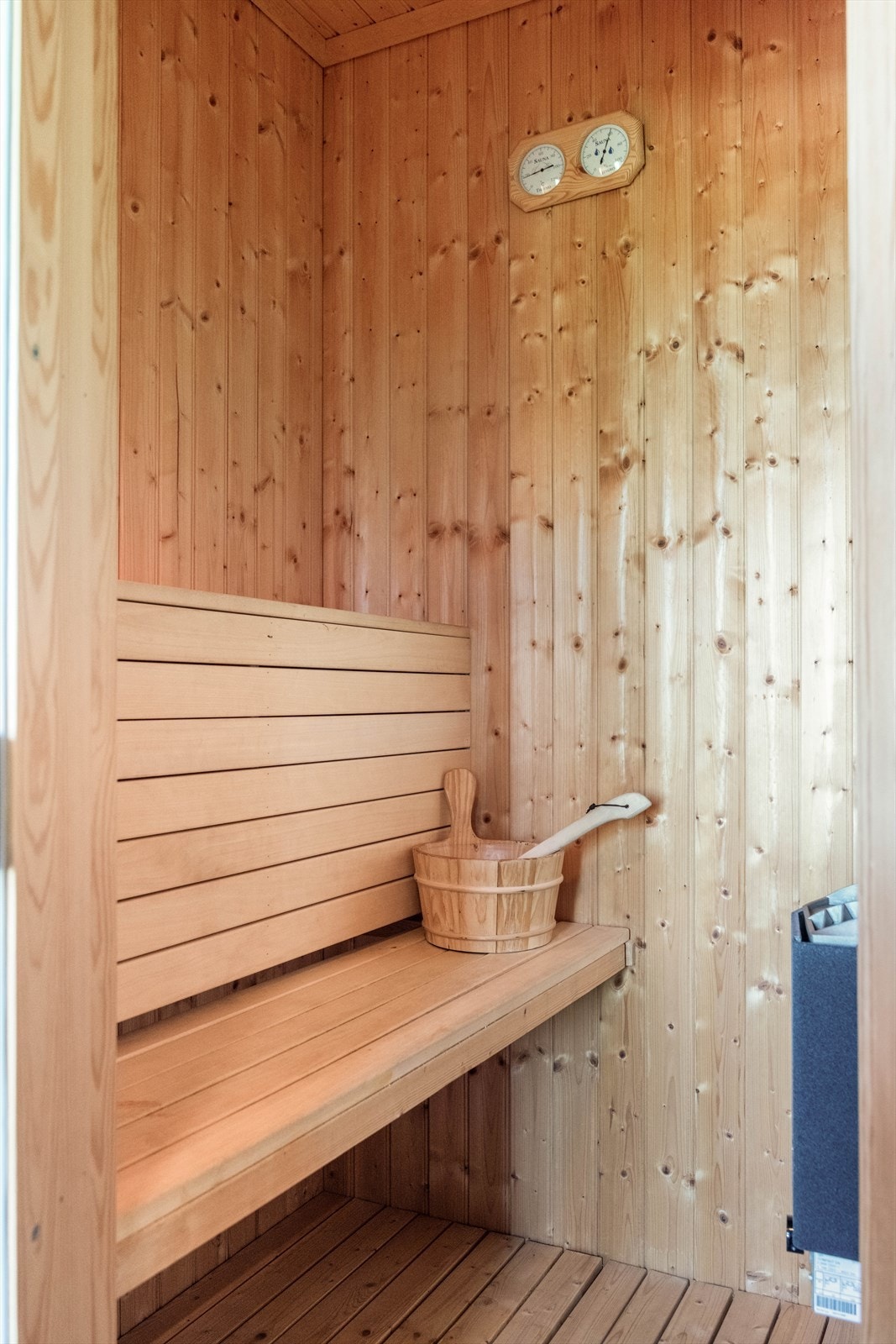 Badstuen har glassdør og trebenker over to plan, med granpanel på vegger og i tak. Galleribilde