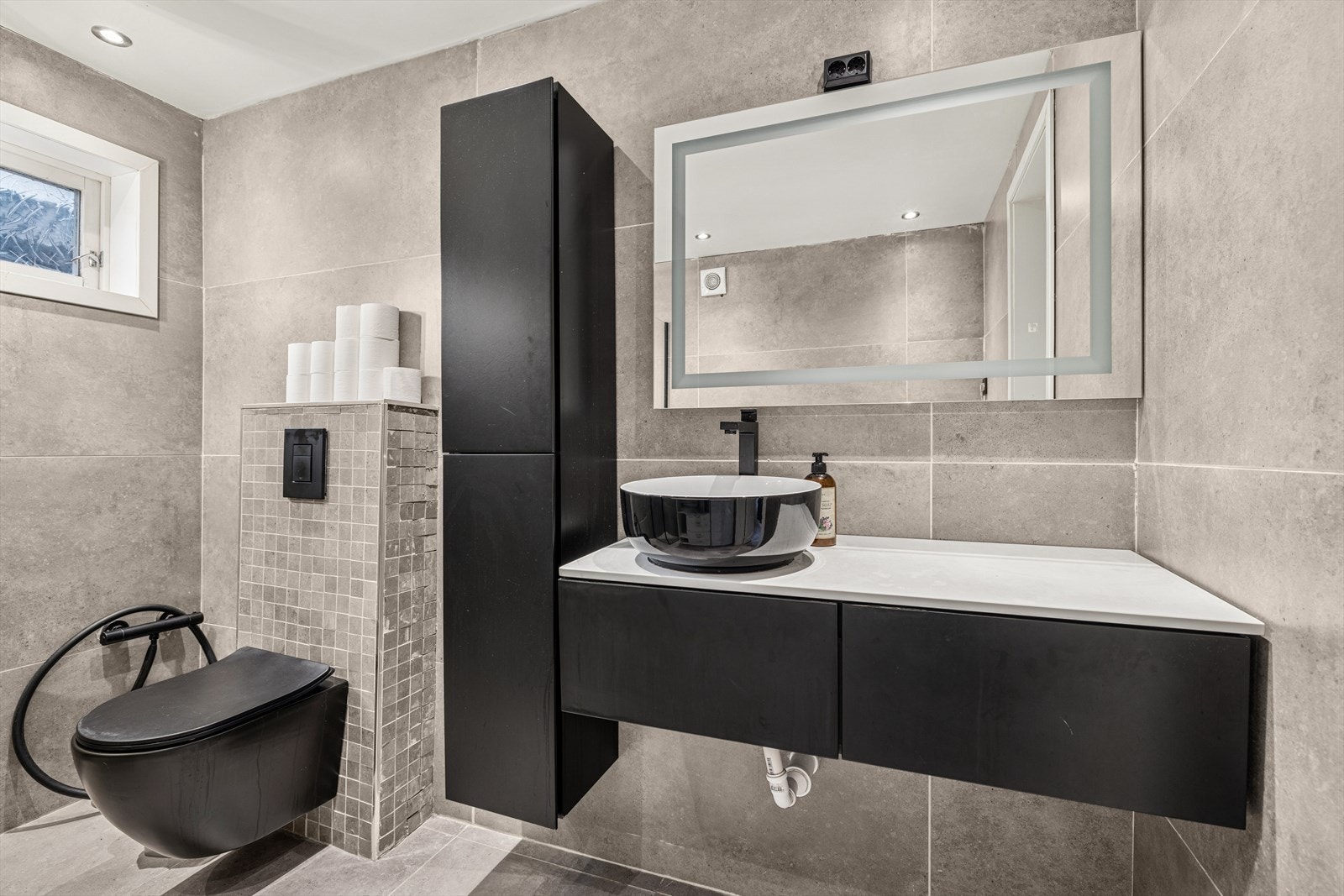 Badet er ellers utstyrt med dusjhjørne, vegghengt toalett og baderomsinnredning med servant. I tillegg har man opplegg for vaskemaskin. Avtrekk via mekanisk vifte. Galleribilde