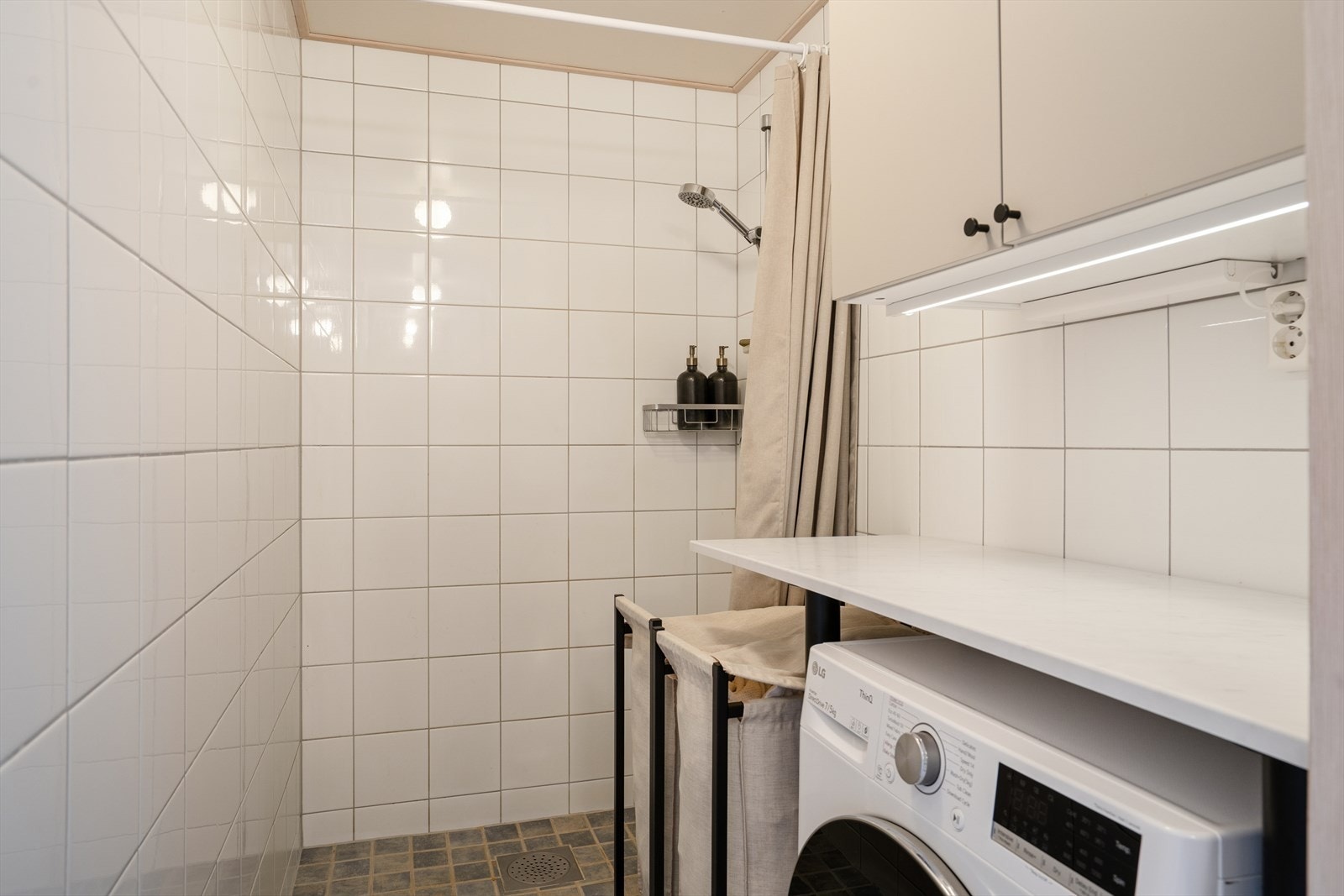 Rommet fremstår lyst og funksjonelt, med flislagte vegger og gulv som gir et moderne og lettstelt uttrykk. Dusjen er etablert direkte på vegg og gulv, noe som gir en åpen og romslig dusjsone. Galleribilde