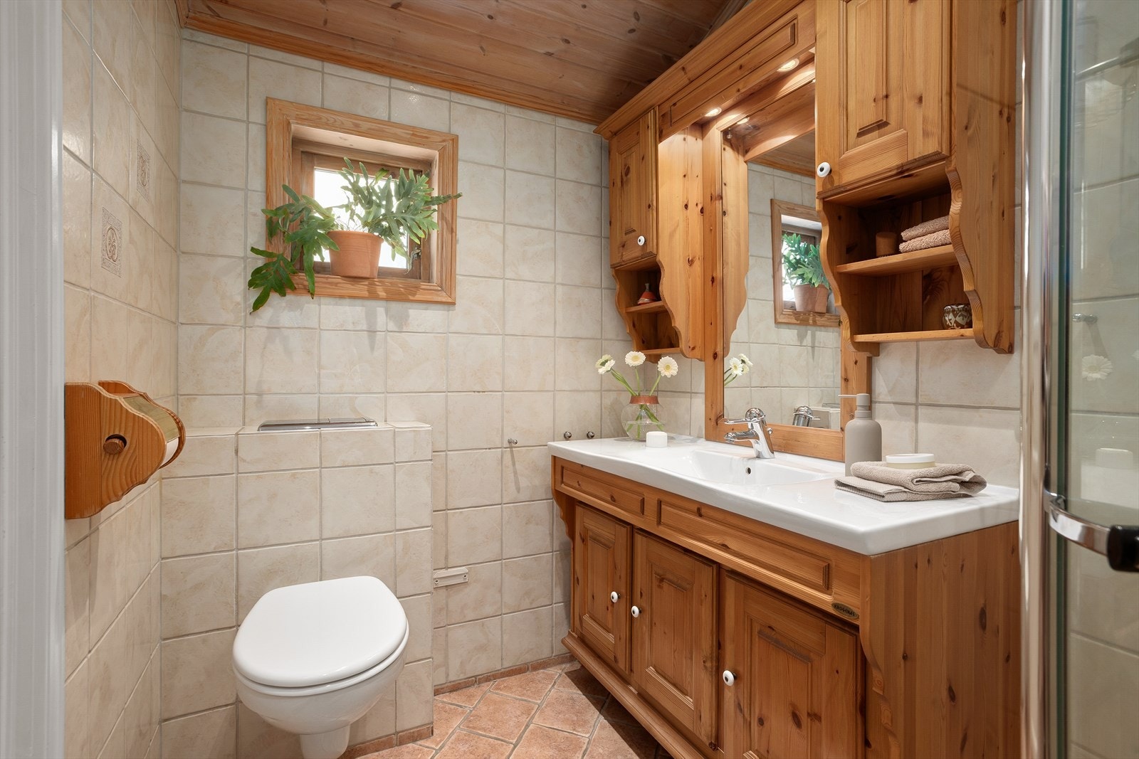 Badet er utstyrt med servant med underskap, veggskap og speil med lys, dusjnisje og vegghengt toalett Galleribilde