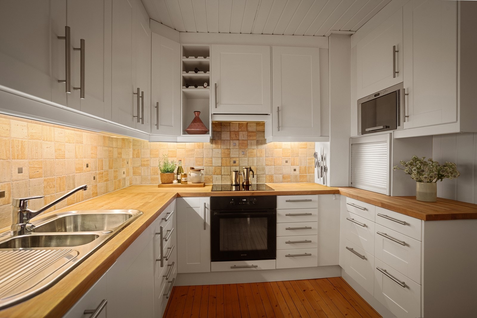 Pent kjøkken med profilerte fronter, flislagt over kjøkkenbenk og benkeplate i heltre Galleribilde